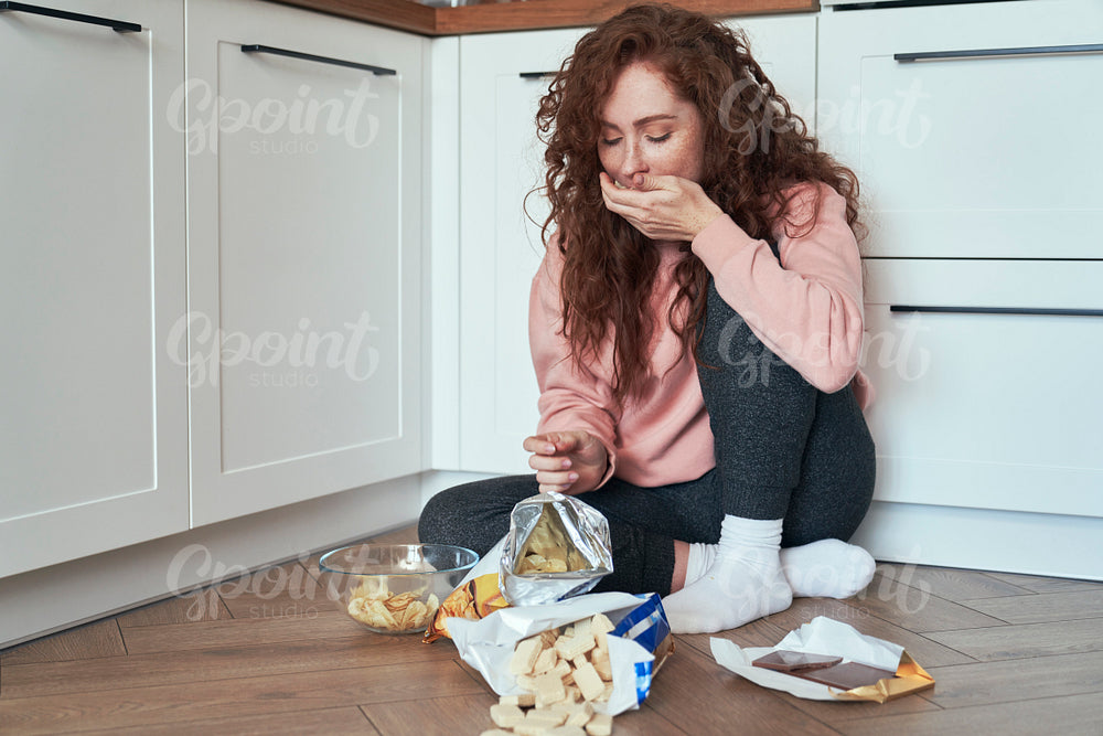 Young caucasian woman having eating disorder and eating greedily on the floor 