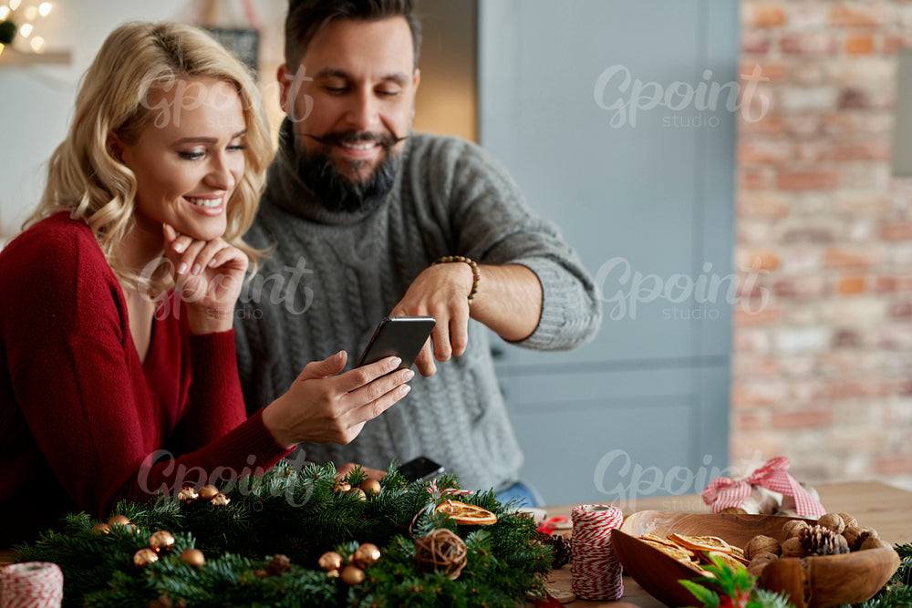 Couple with a Christmas wreath watching something on a phone
