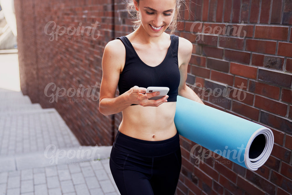 Smiling woman with mobile phone and exercise mat