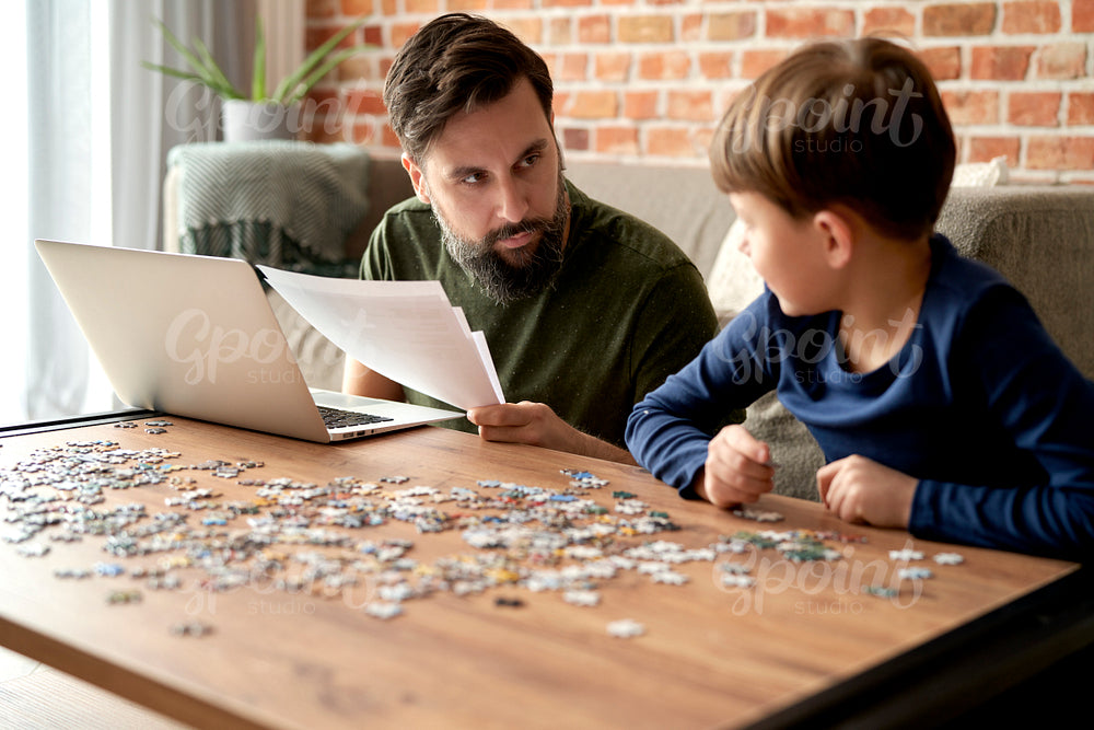 Father working and son solving jigsaw puzzle