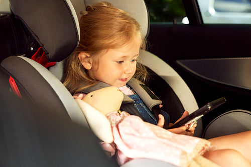 Cute little girl sitting in the baby car seat with phone