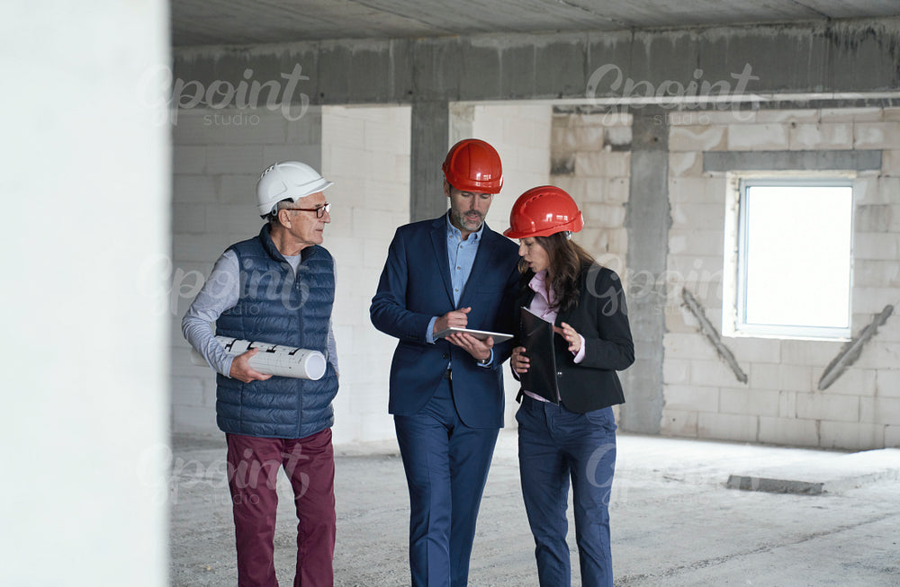 Wide image of group of caucasian engineers and investors walking and discussing on construction site 