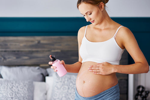 Young pregnant women applying cream on her belly