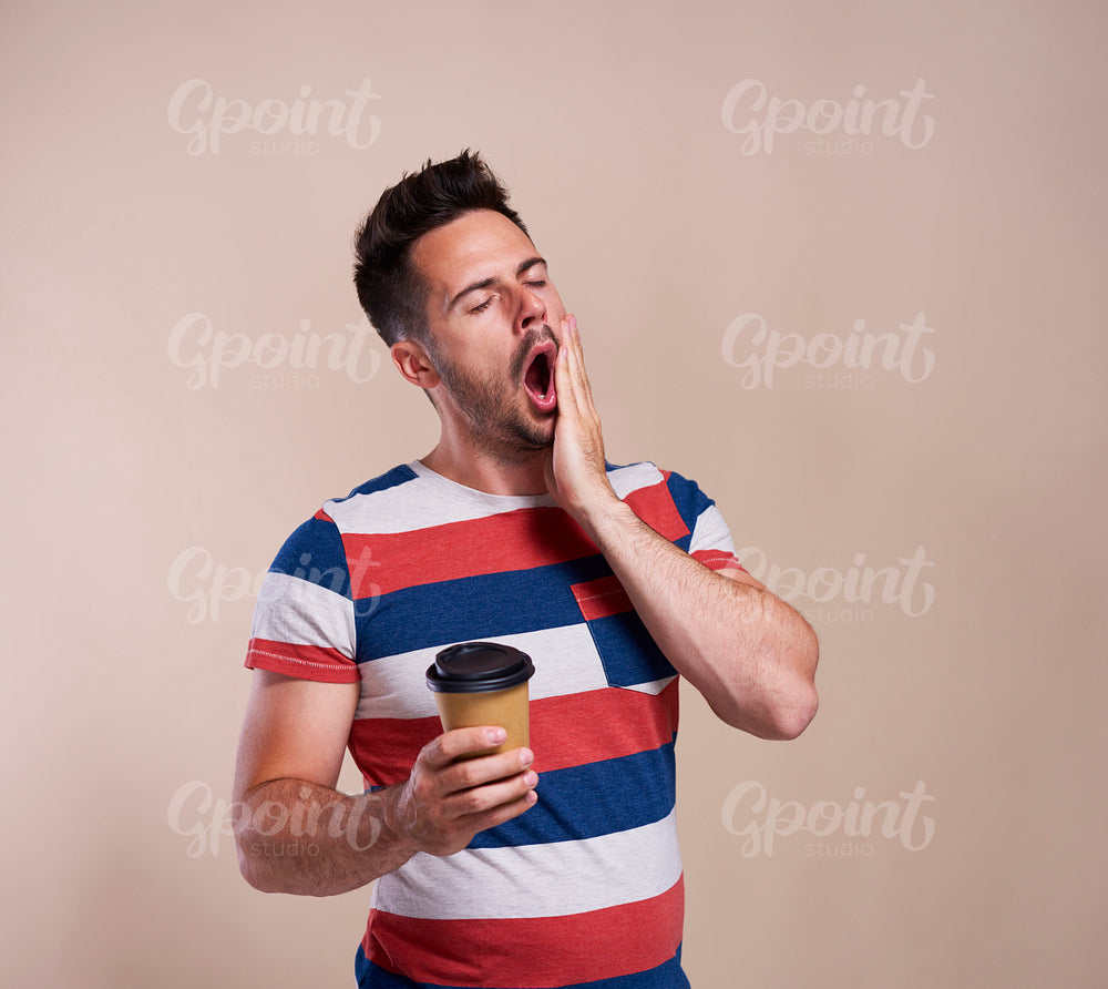 Tired man yawning and holding disposable cup of coffee