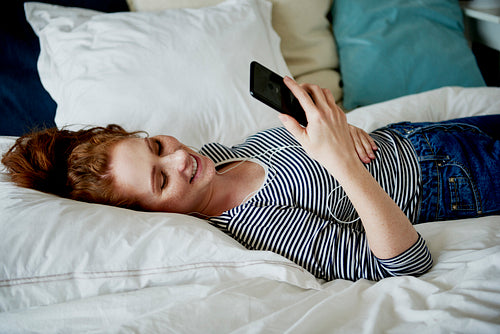 Woman browsing mobile phone while lying on the bed
