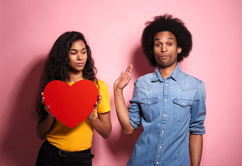 Young African couple holding a red heart with negative emotions.
