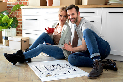 Portrait of smiling couple in their new apartment with blueprint
