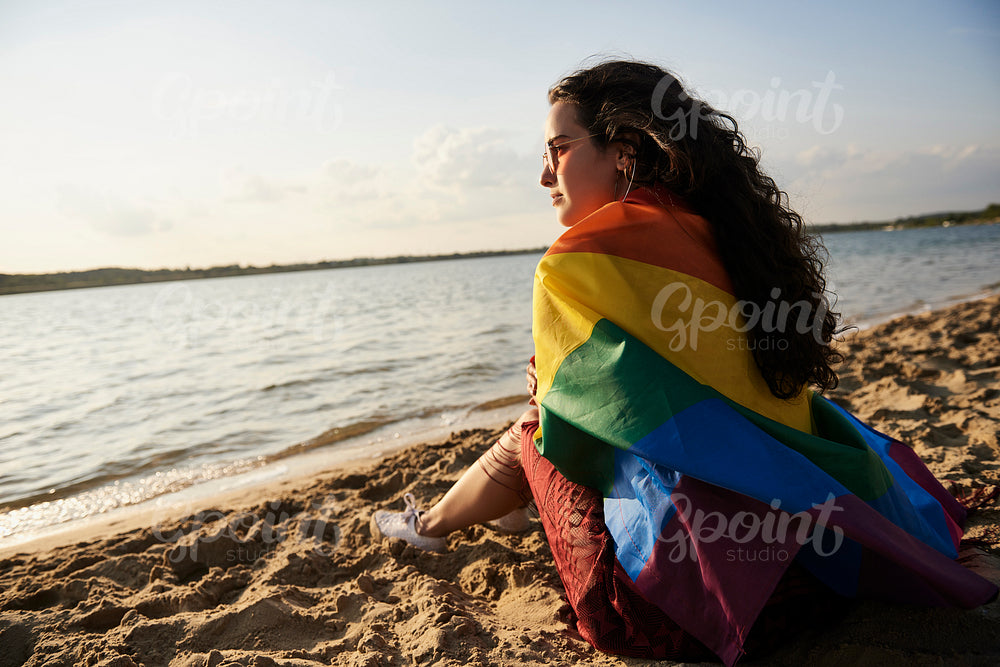 Girl sitting on the beach and watching sunset with rainbow flag