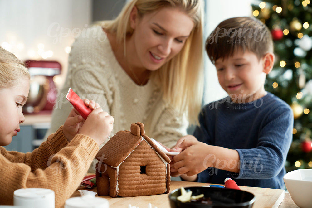 Happy children decorating gingerbread house with their mom