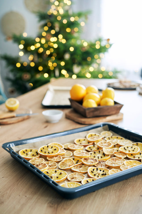 Dried lemons and oranges on baking tray and Christmas tree in the background