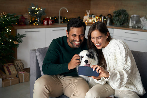 Happy multi ethnicity couple make selfie with dog at home during the Christmas