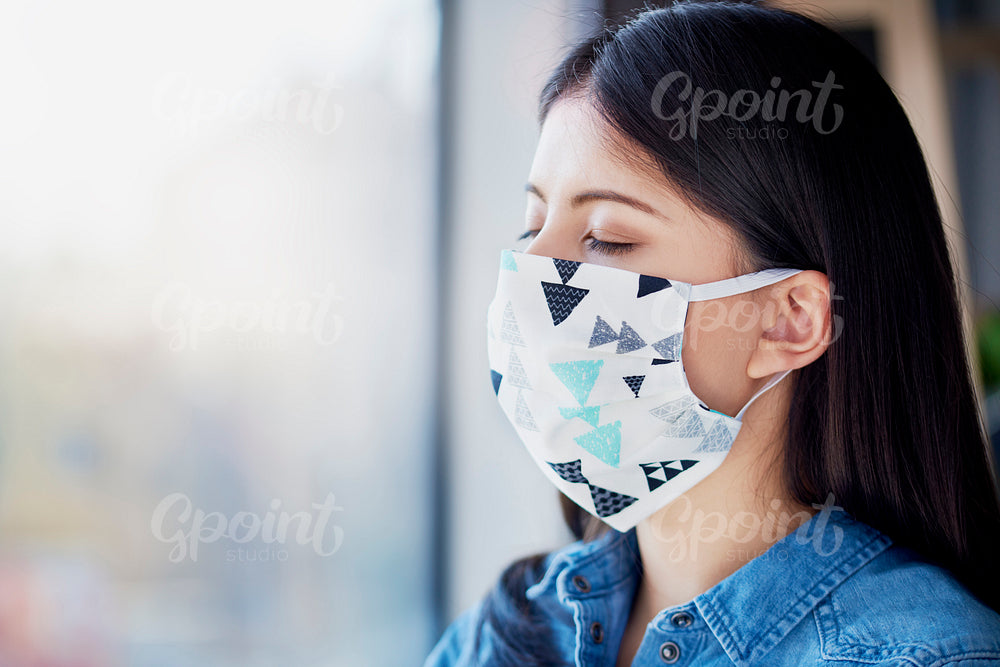 Woman in protective mask relaxing next to the window