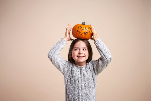 Playful girl holding halloween pumpkin on her head