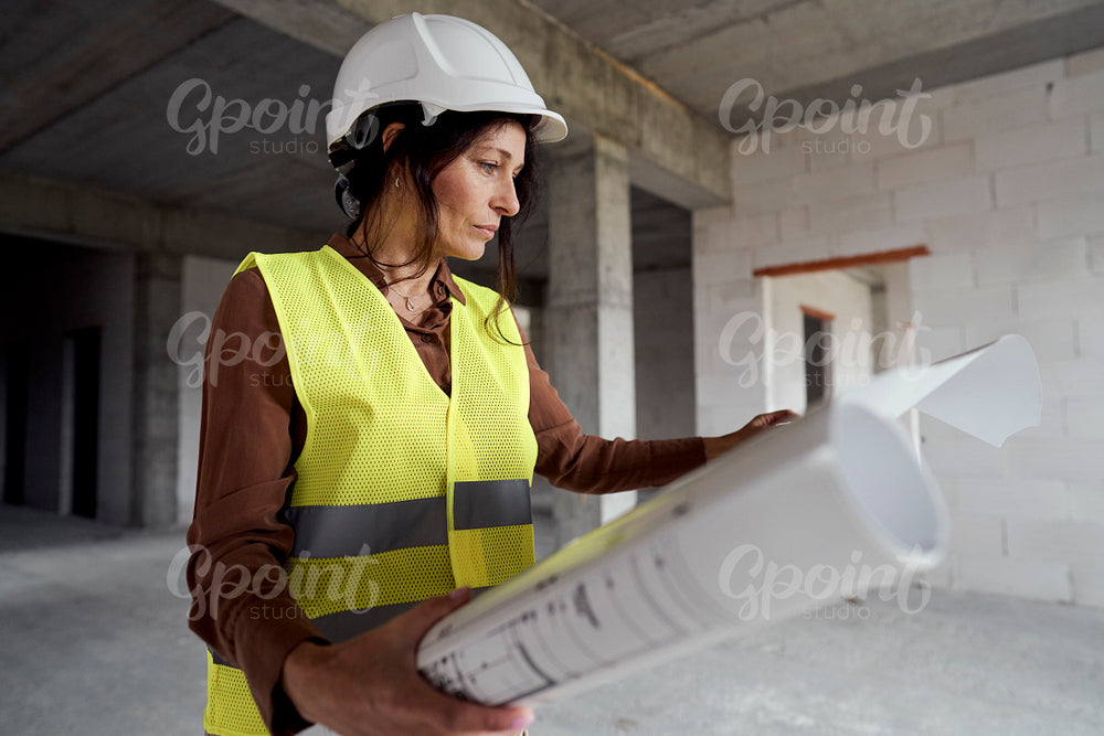 Female mature caucasian engineer standing on construction site and browsing building plans   