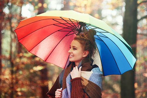Beautiful woman with a rainbow umbrella in the autumnal forest