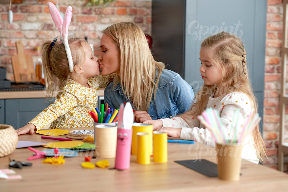 Cute kissing mom with daughters during preparing Easter decorations