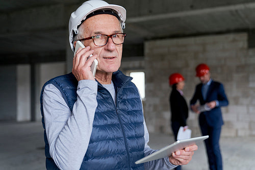 Senior investor man standing in front and discussing by mobile phone on construction site