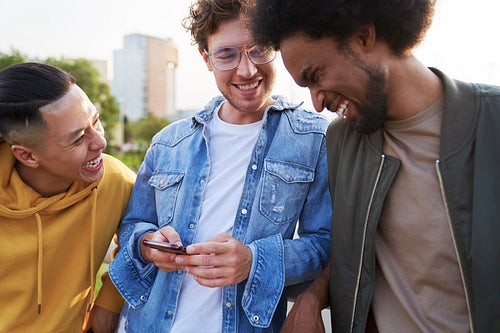 Three young men laughing at something holding mobile phone
