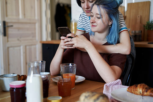 Lesbian couple browsing something on the phone in the kitchen