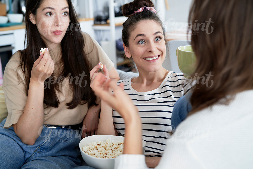 Surprised friends talking and eating popcorn