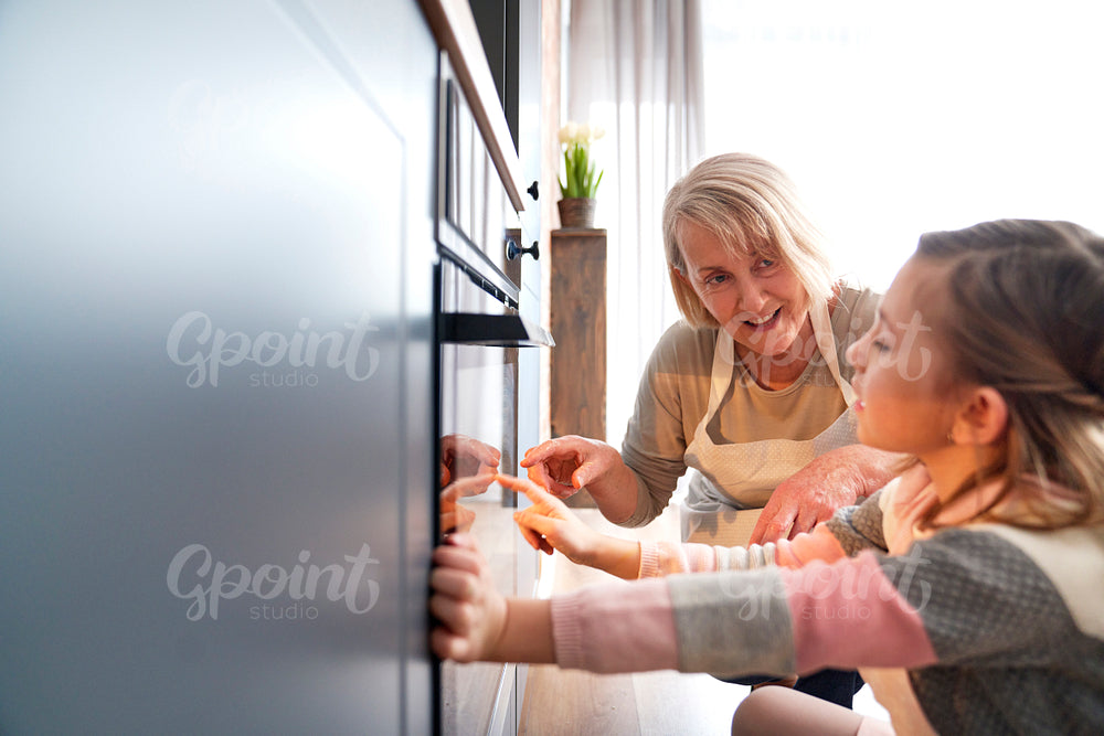 Girl and grandmother watching easter biscuits in kitchen oven