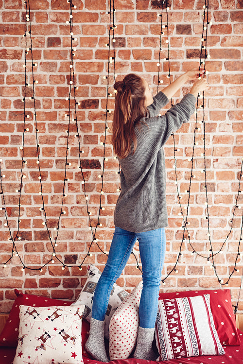 Woman standing on bed and hanging christmas lights