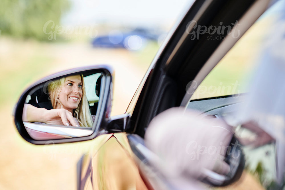 Reflection in wing mirror of smiling woman driving car