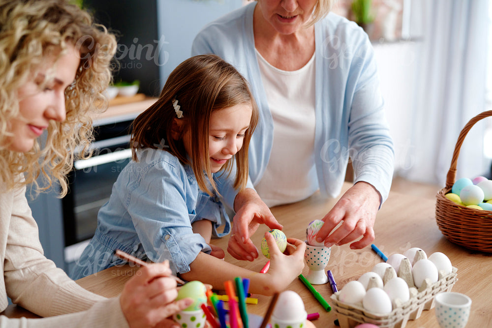 Mother grandmother and granddaughter decorate easter eggs together