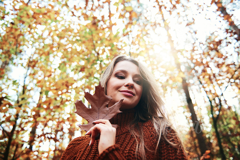 Beautiful smiling young woman holding autumnal leaf