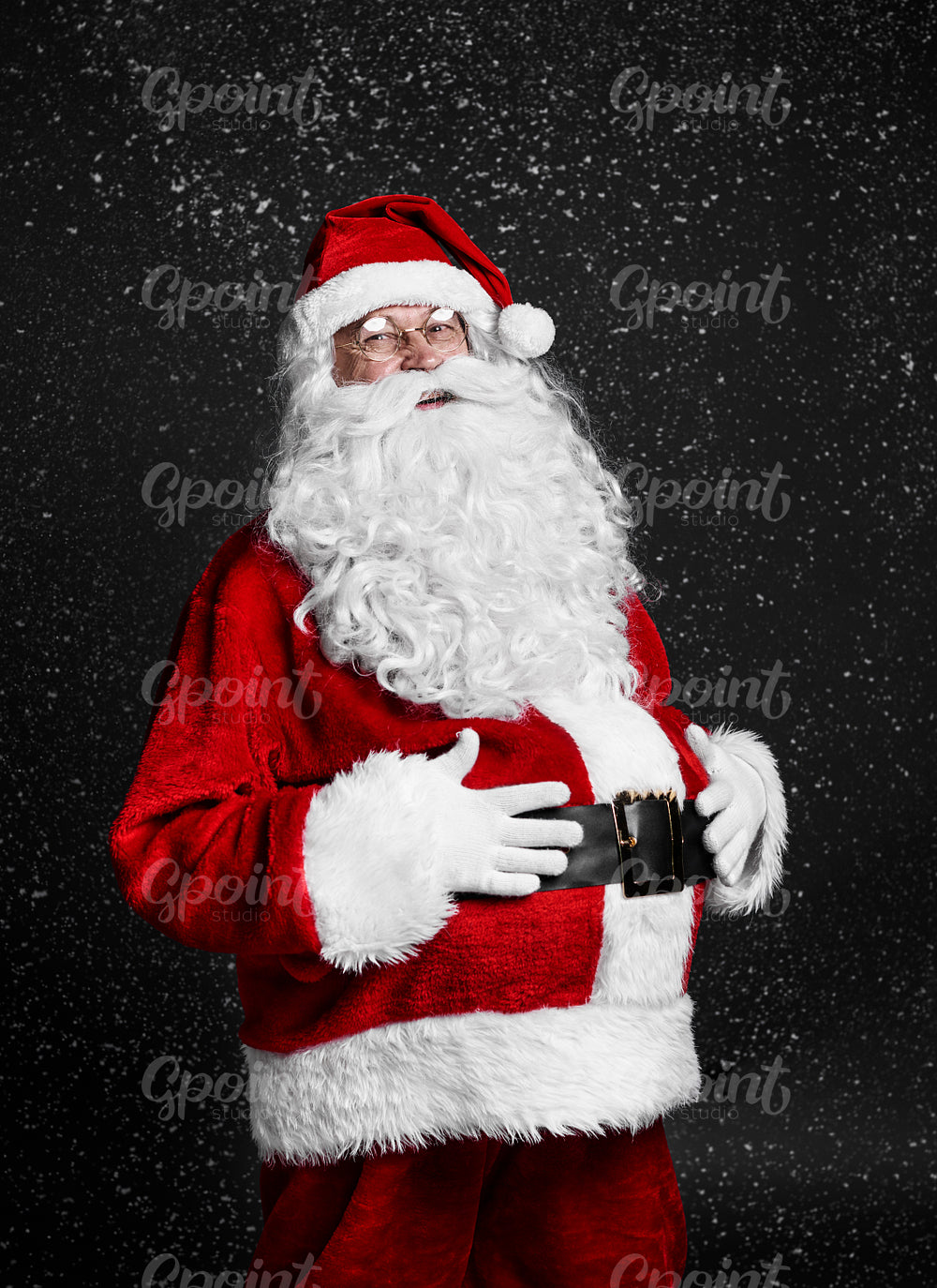 Cheerful santa claus touching his belly among snow falling