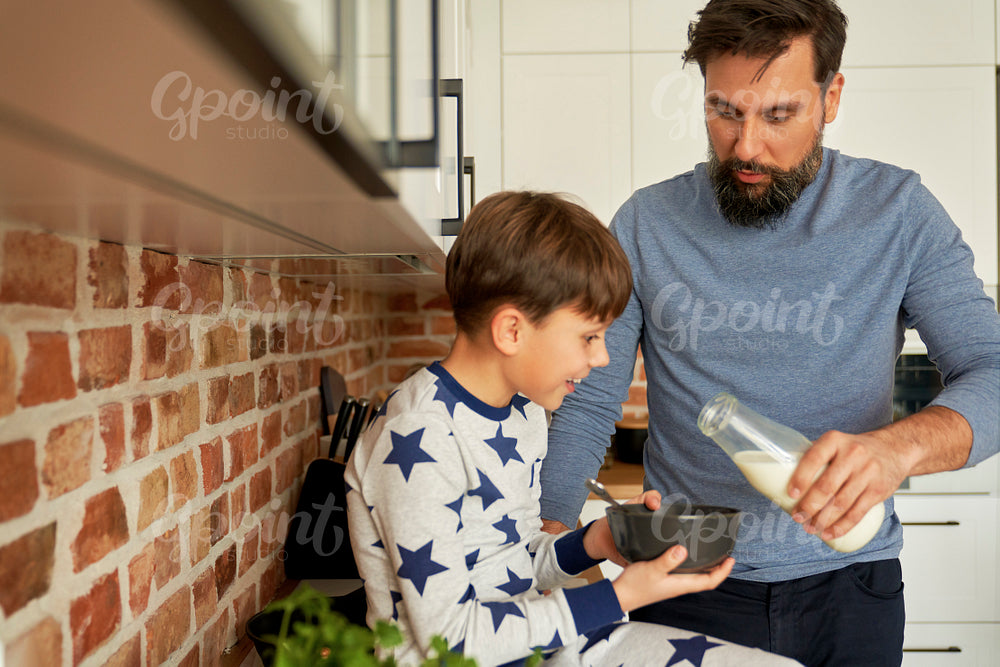 Father pours milk into breakfast cereal for his son