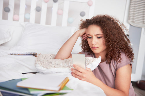 Worried teenage girl using a smart phone in her bedroom