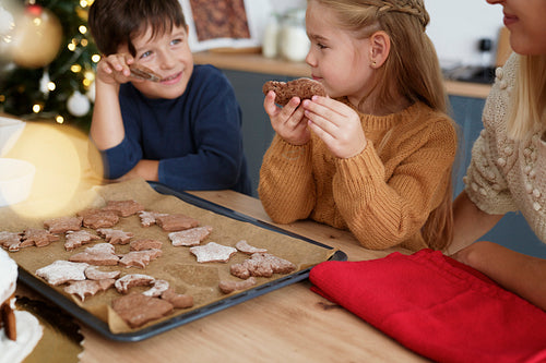 Children tasting homemade cookies baked with mother
