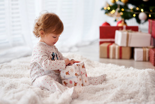 Side view of charming baby opening Christmas gift