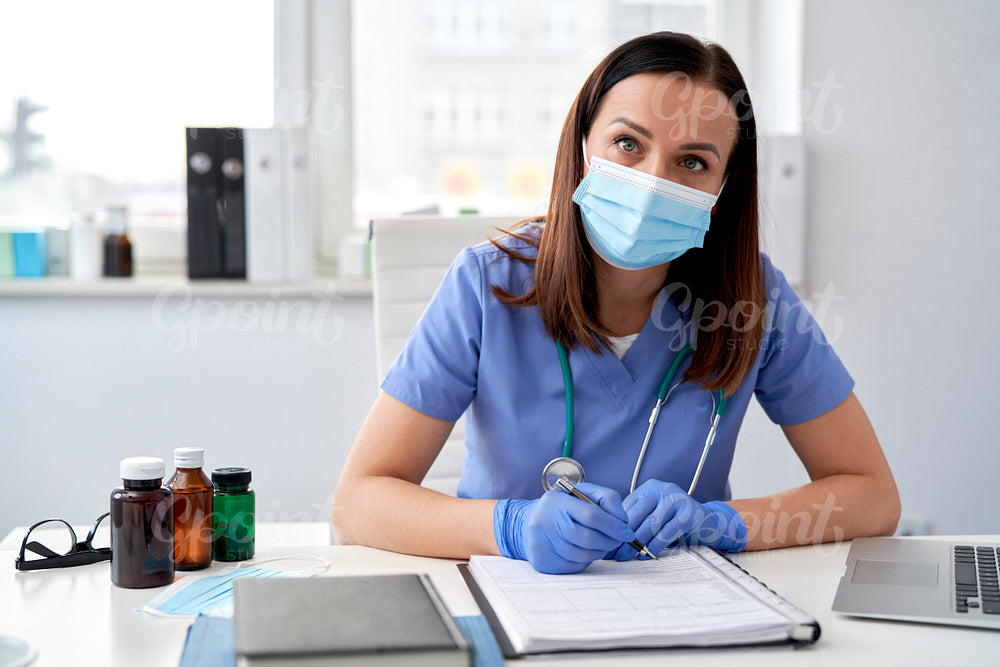 Portrait of female doctor sitting at desk in protective mask
