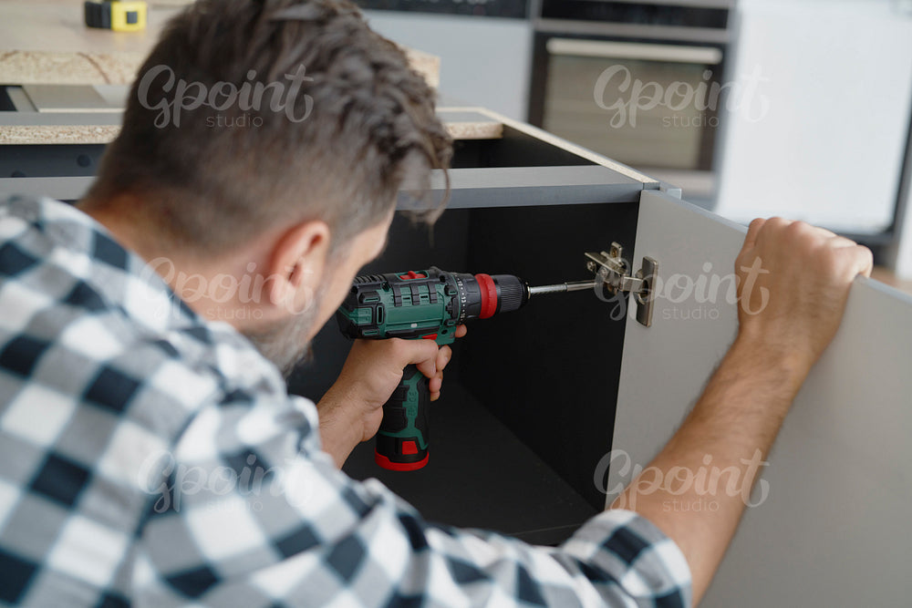 Man installing hinges in kitchen furniture