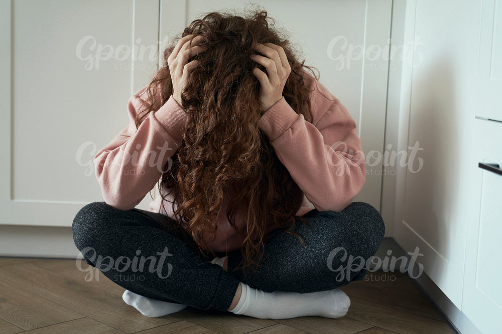 Broken young caucasian woman  with hidden face sitting on floor in the kitchen