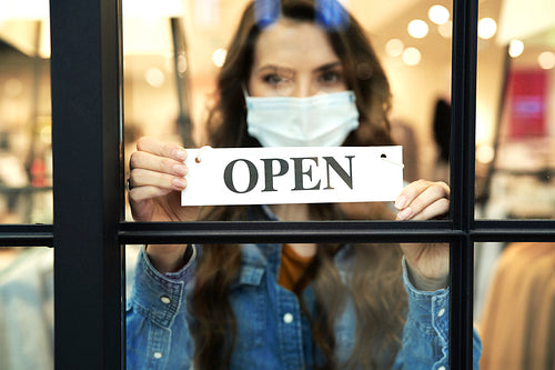 Woman holding Open sign in a small business boutique shop