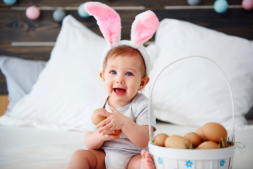 Portrait of baby with bunny ears holding eggs