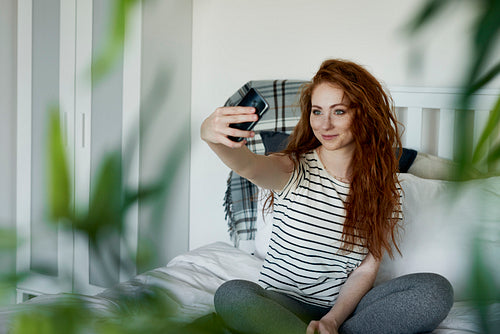 Attractive woman taking selfie while sitting on bed