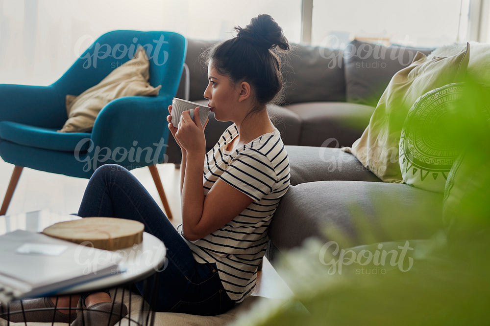 Side view of woman sitting on the floor and drinking something.