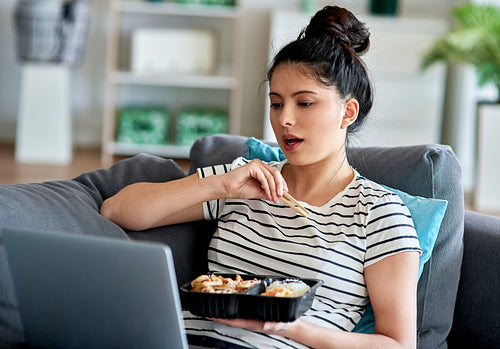 Young Asian woman eating lunch during video conference at home.