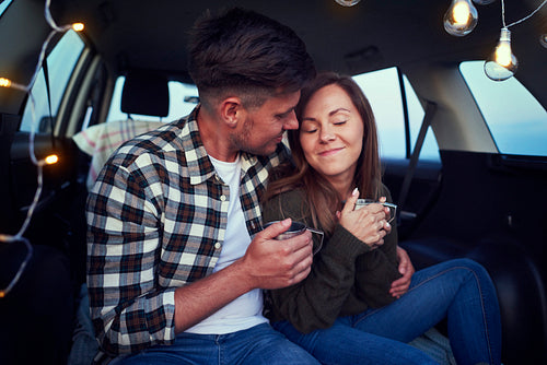Young couple embracing and drinking coffee in car
