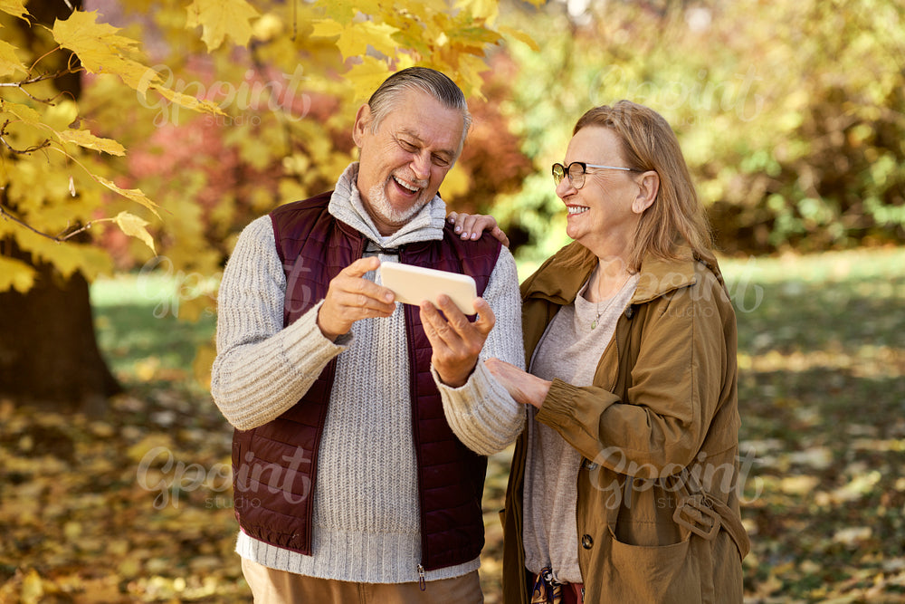 Senior woman and man looking at mobile phone at the park in autumn 