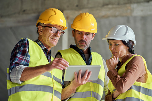 Three caucasian engineers discussing over digital tablet on the construction site