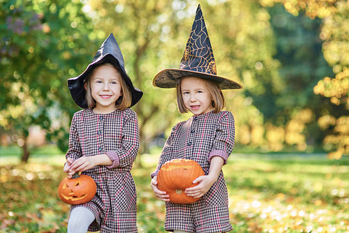 Charming kids in witch costume holding halloween pumpkins
