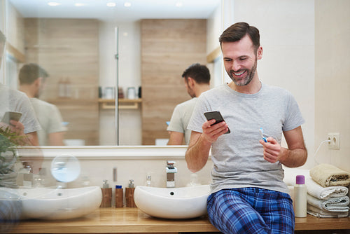 Man brushing teeth and using mobile phone in the bathroom