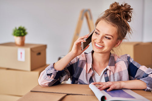 Happy woman talking by mobile phone among boxes