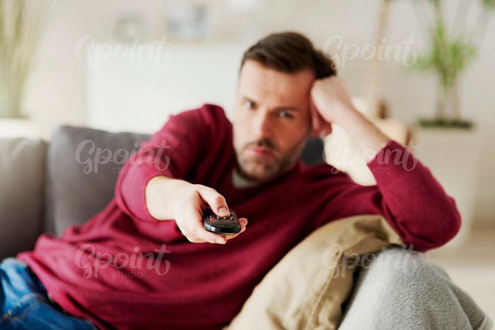 Bored man holding a remote and watching TV