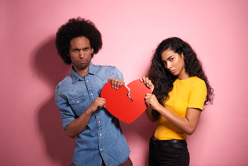 Sad African couple breaking the red heart in studio shot.